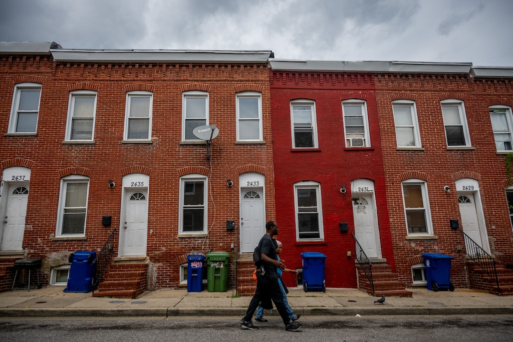 Photo of Baltimore row houses from street. A duo walks on sidewalk.